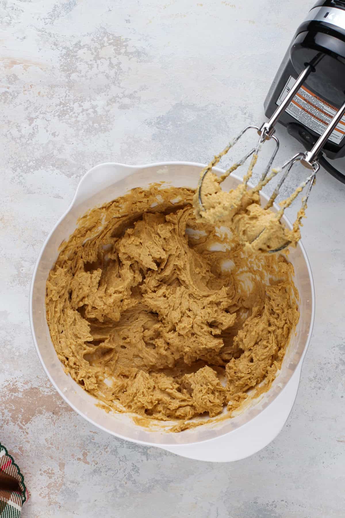 Wet ingredients for gingersnaps mixed by an electric mixer in a white bowl.