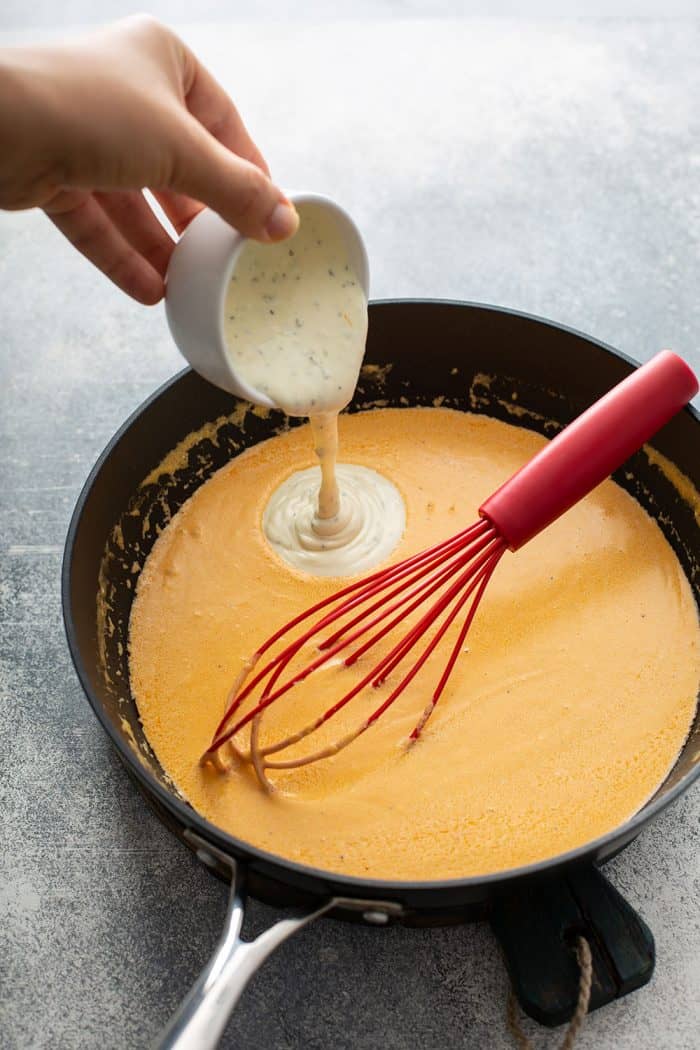 Hand pouring ranch dressing into a saucepan with the sauce for buffalo chicken dip