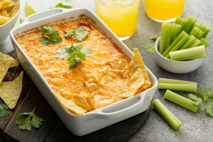 White casserole dish with buffalo chicken dip next to celery sticks on a concrete counter