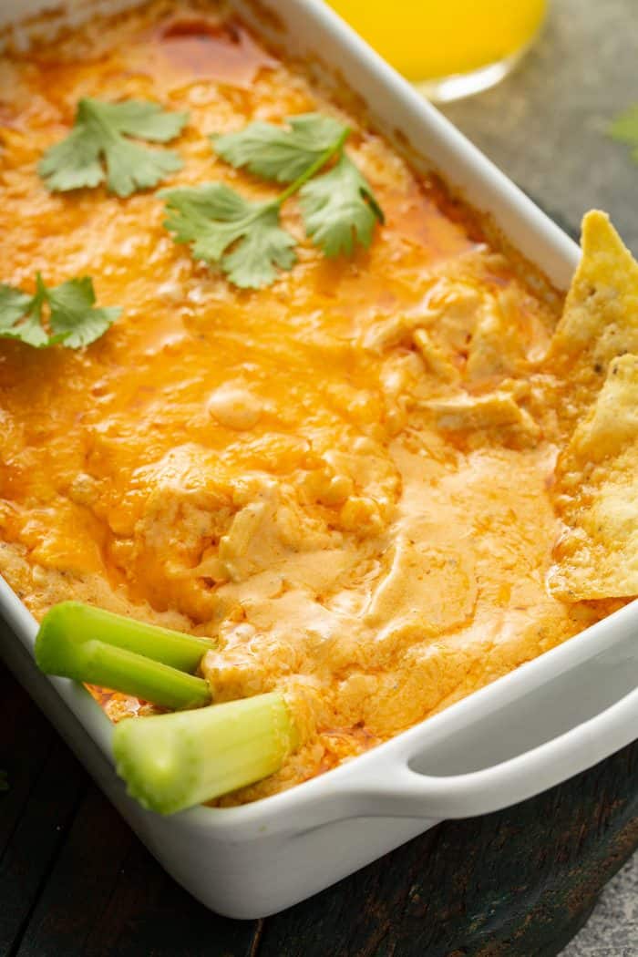 Celery sticks and tortilla chips sticking out of buffalo chicken dip in a white casserole dish