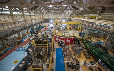 View from near ceiling shows NCNR guide hall filled with big pieces of scientific equipment, including several long cylindrical "guides" running toward the far end of the room. 