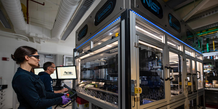 NIST researchers Elizabeth Strychalski and David Ross program the robotic arm that operates within the box-like structure of the NIST biofoundry.