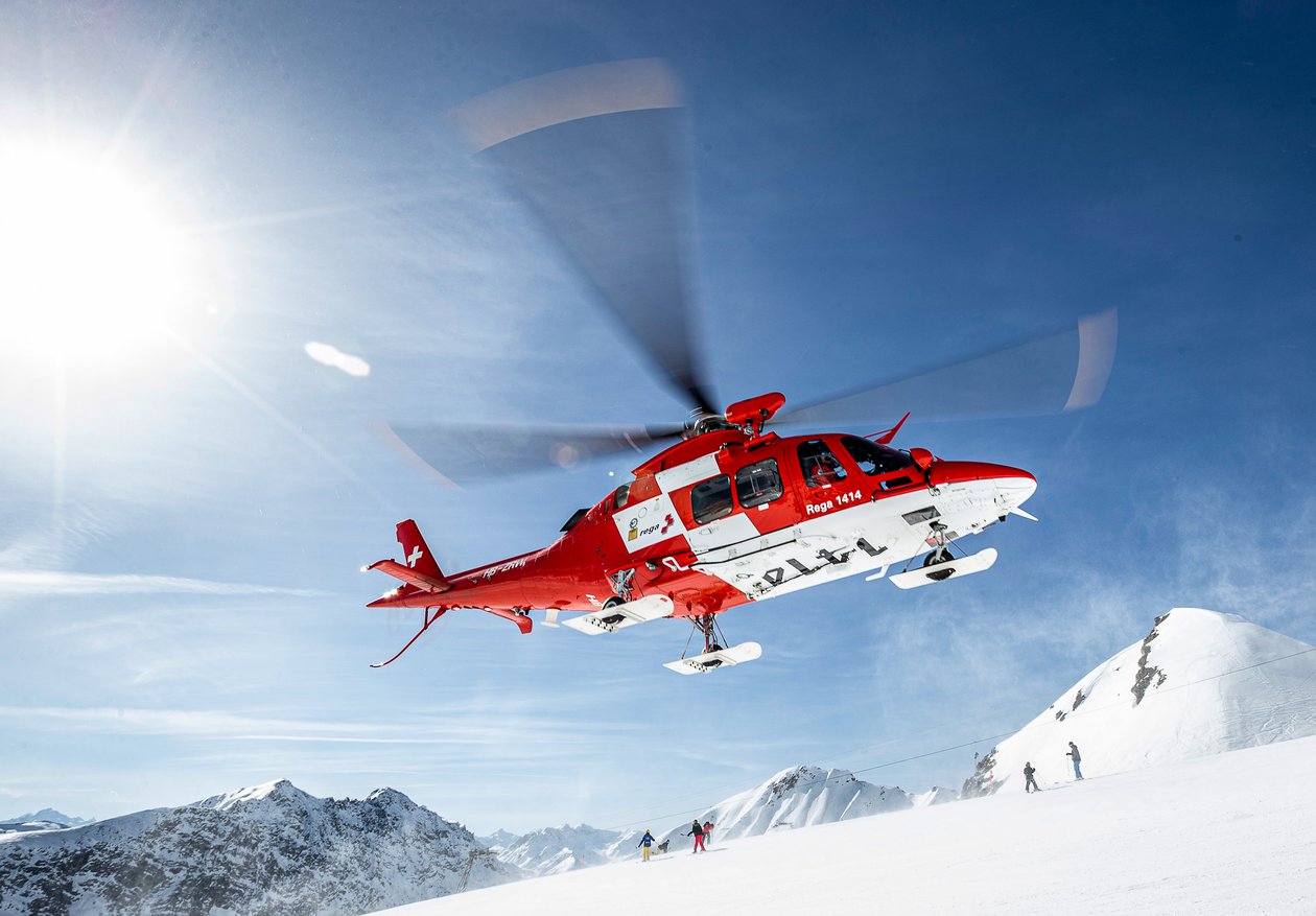 Rettungshelikopter AgustaWestland vor blauem Himmel und schneebedeckten Bergen