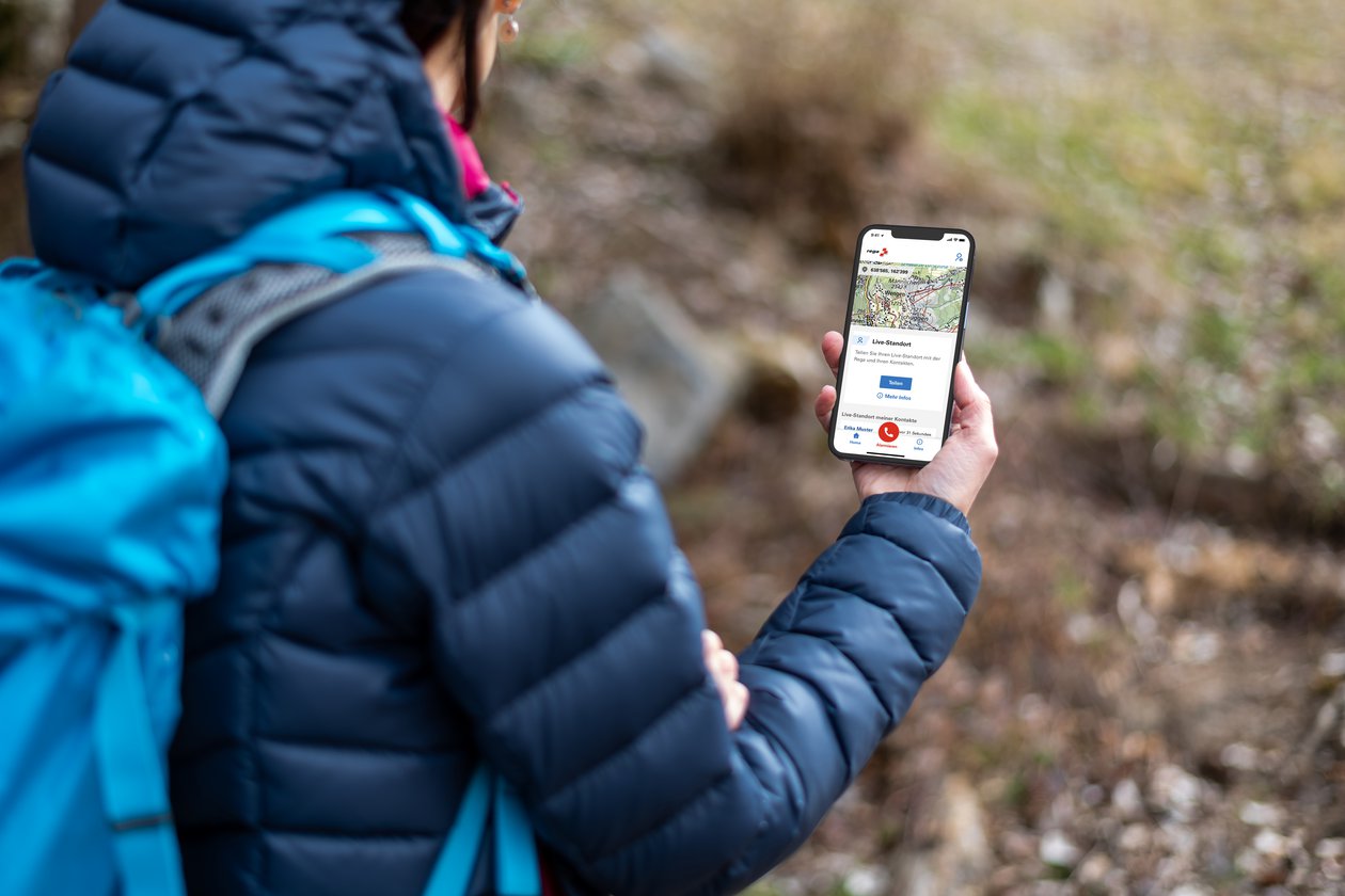 Wanderin hält ein Handy, auf dem die Rega-App geöffnet ist.