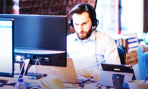 Imagen de un jóven revisando atentamente su computador y utilizando unos auriculares