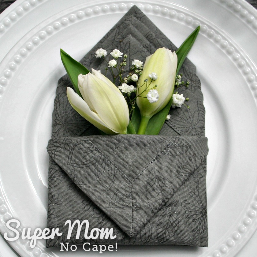 Two white tulips and some baby's breath in the grey napkin pocket