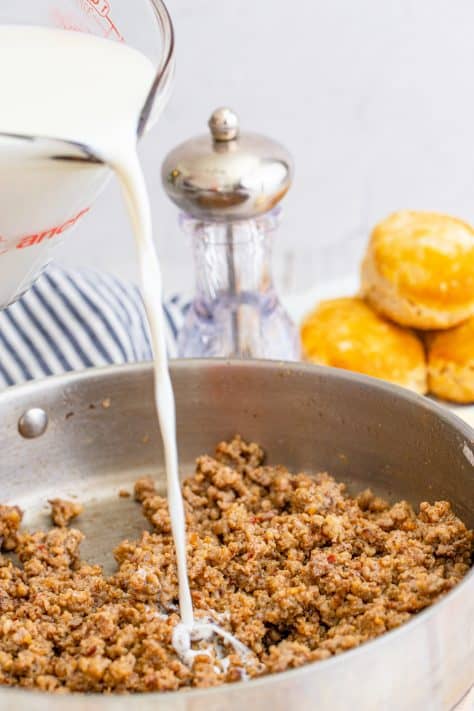 Milk being poured into cooked sausage in metal pan