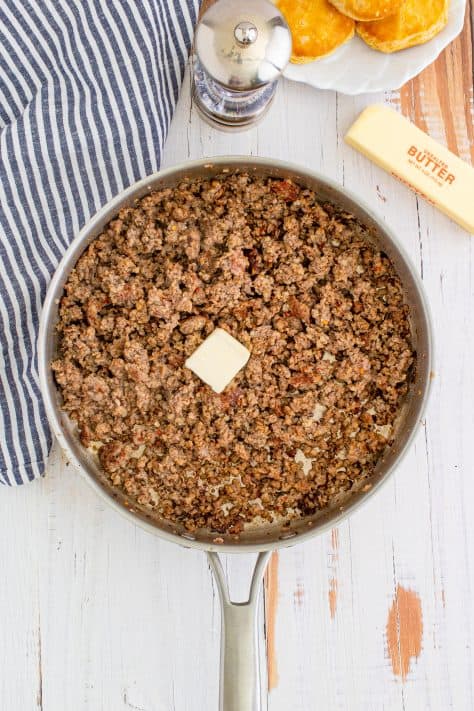 Butter added to cooked sausage in metal pan with striped linen