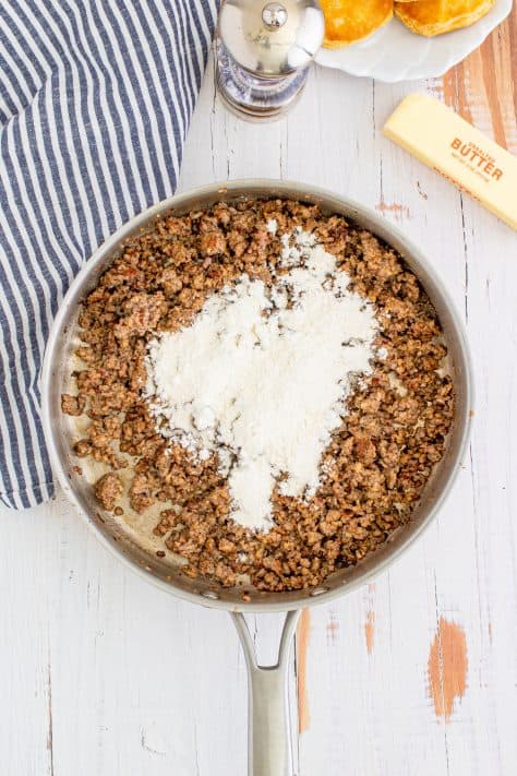 Flour sprinkled over cooked sausage in metal pan with striped linen