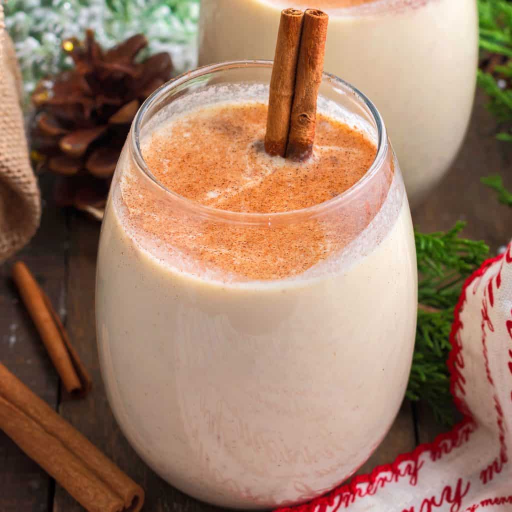 Square image close up of Homemade Eggnog in glass with cinnamon stick.