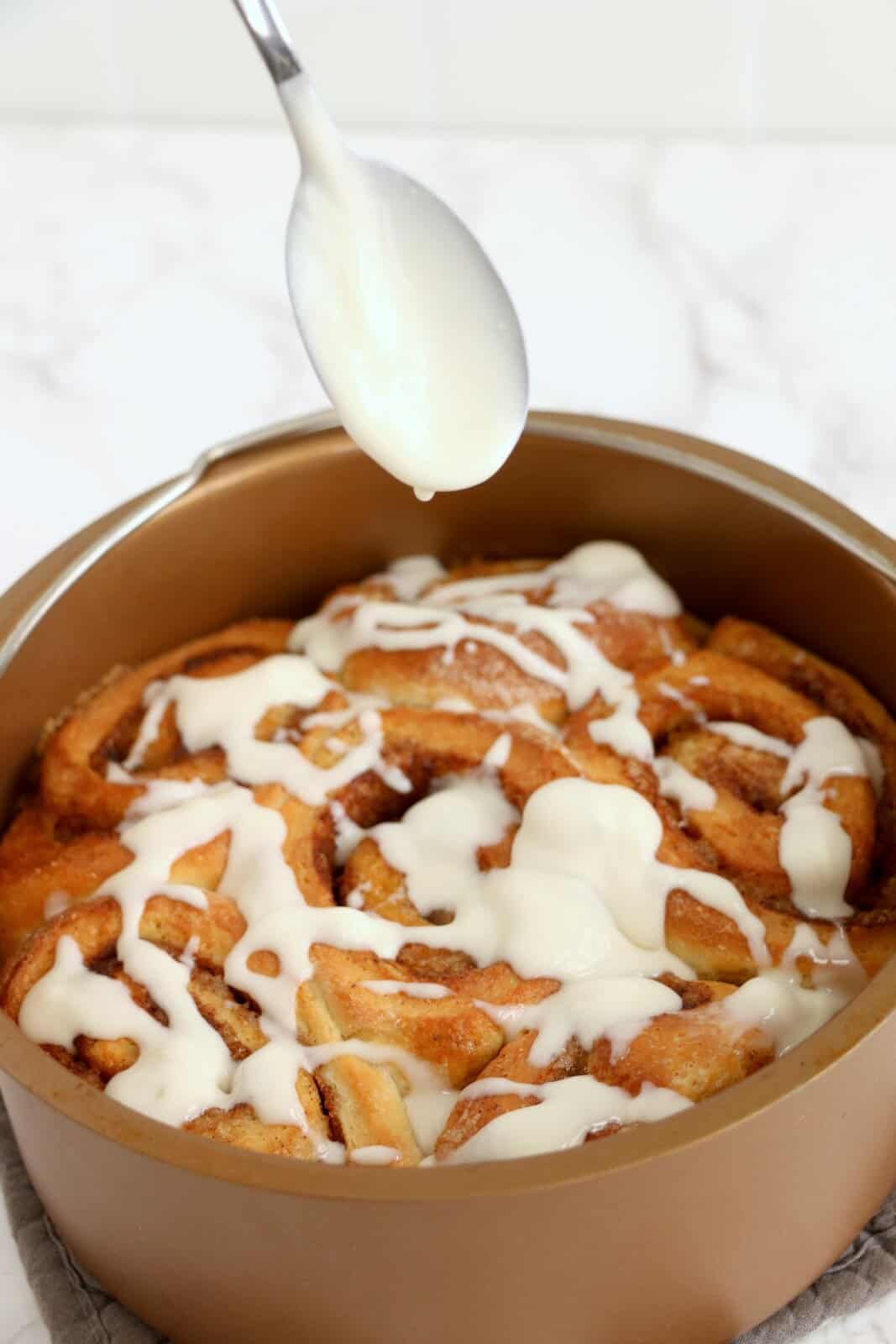 Icing being drizzled over cinnamon rolls.