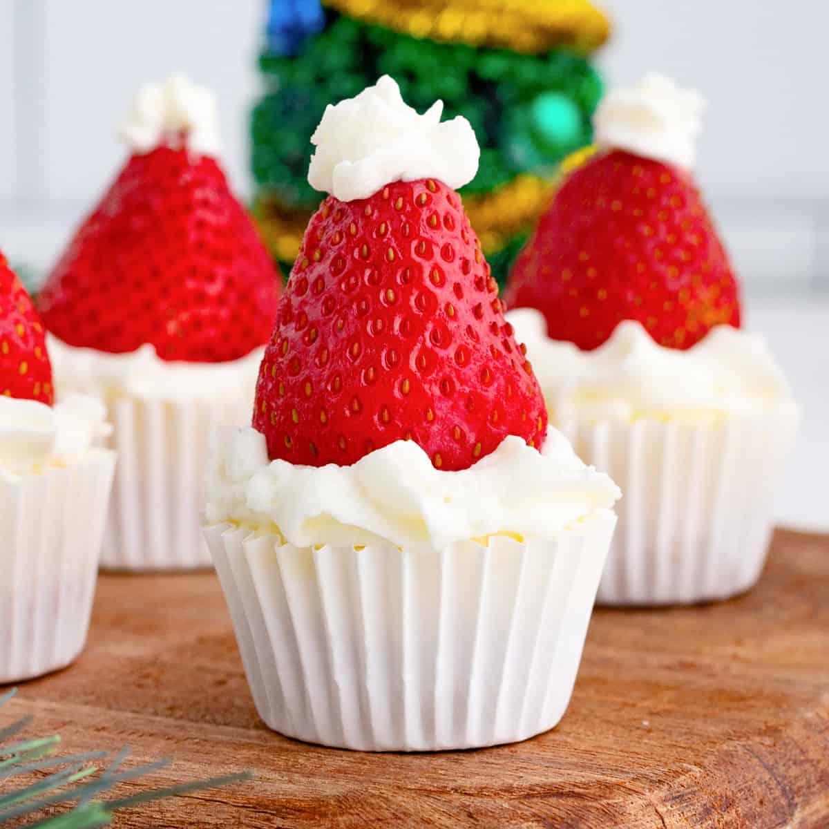 Close up square image of Santa Hat Mini Cheesecakes on wooden board garnished.