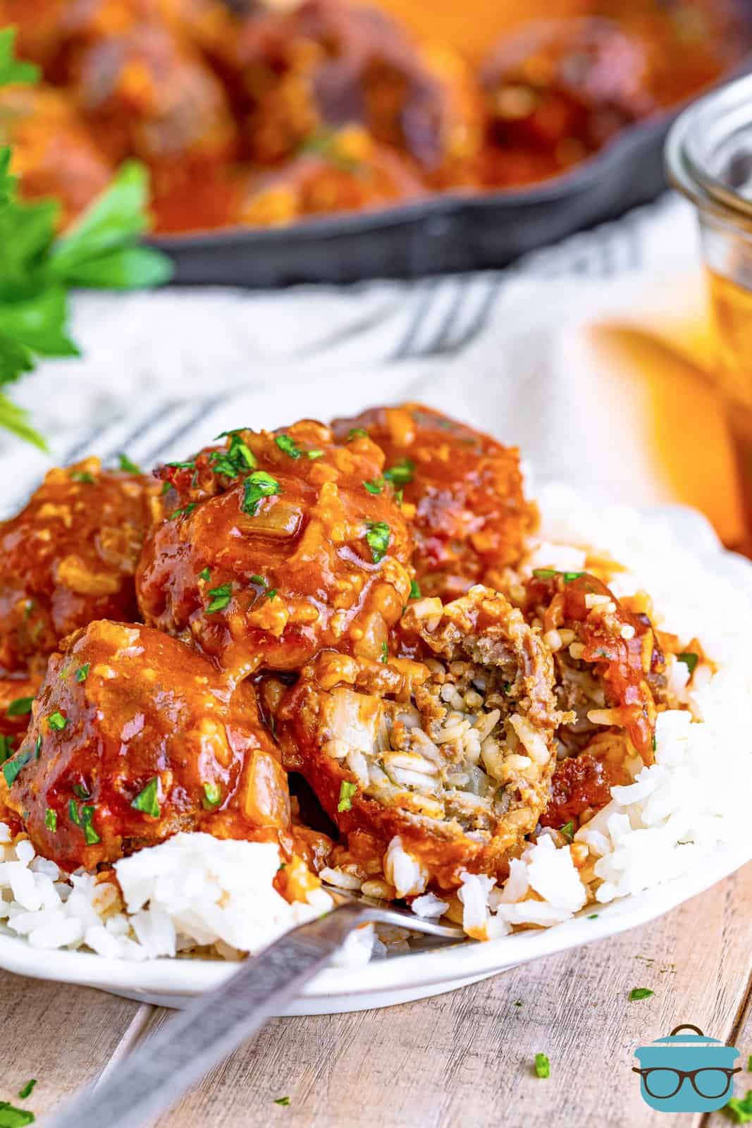 A plate of rice with meatballs on top and one bite taken out of one.