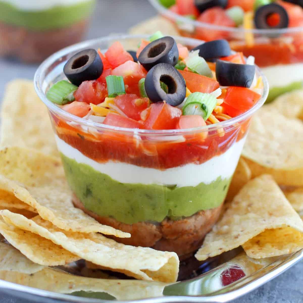 Seven layer dip in clear plastic cups with chips on a cup.