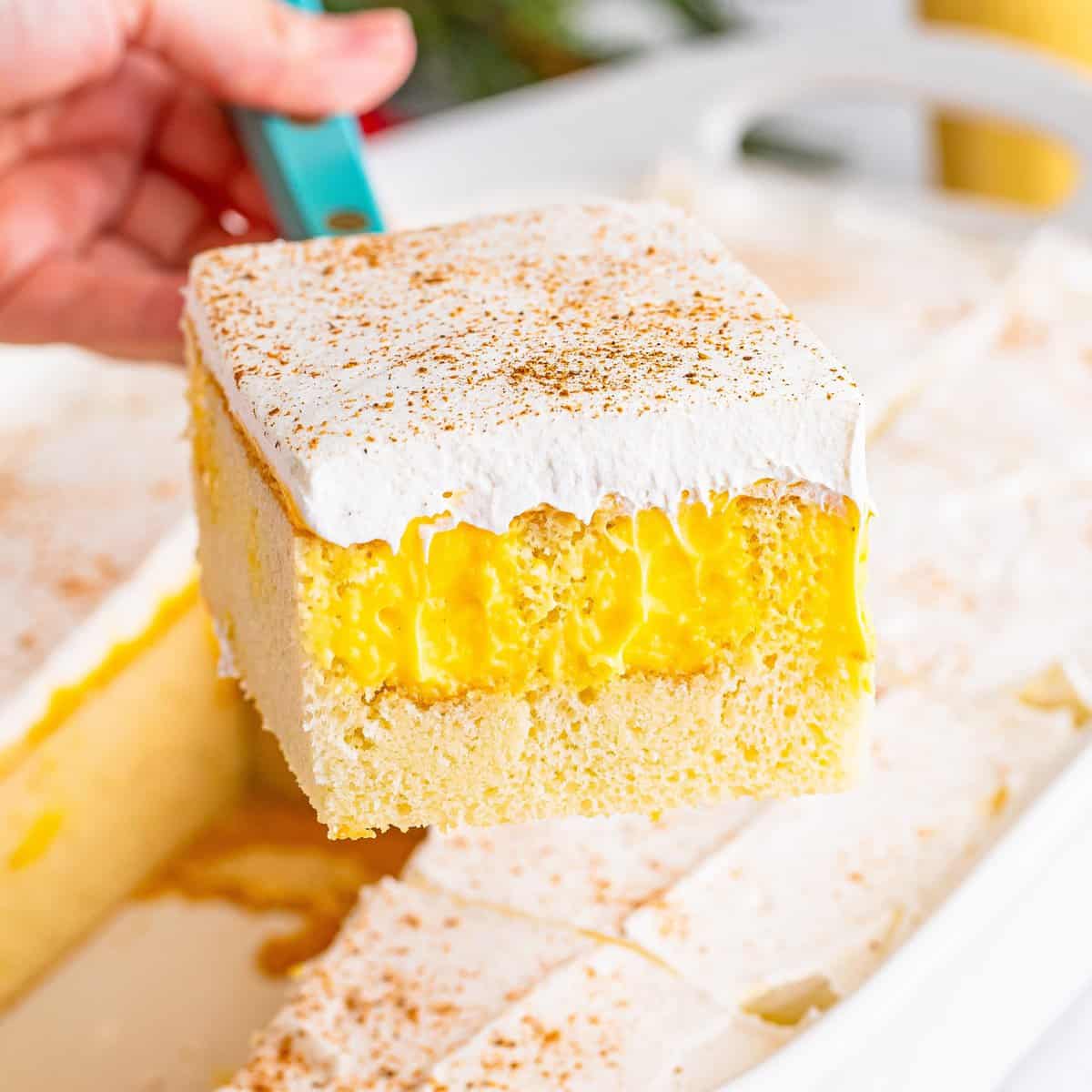 A utensil holding a slice of Eggnog Poke Cake above the rest of the cake.