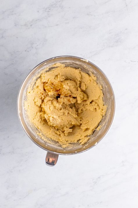 Vanilla extract being added to creamed butter, sugar, and flour in a mixing bowl.