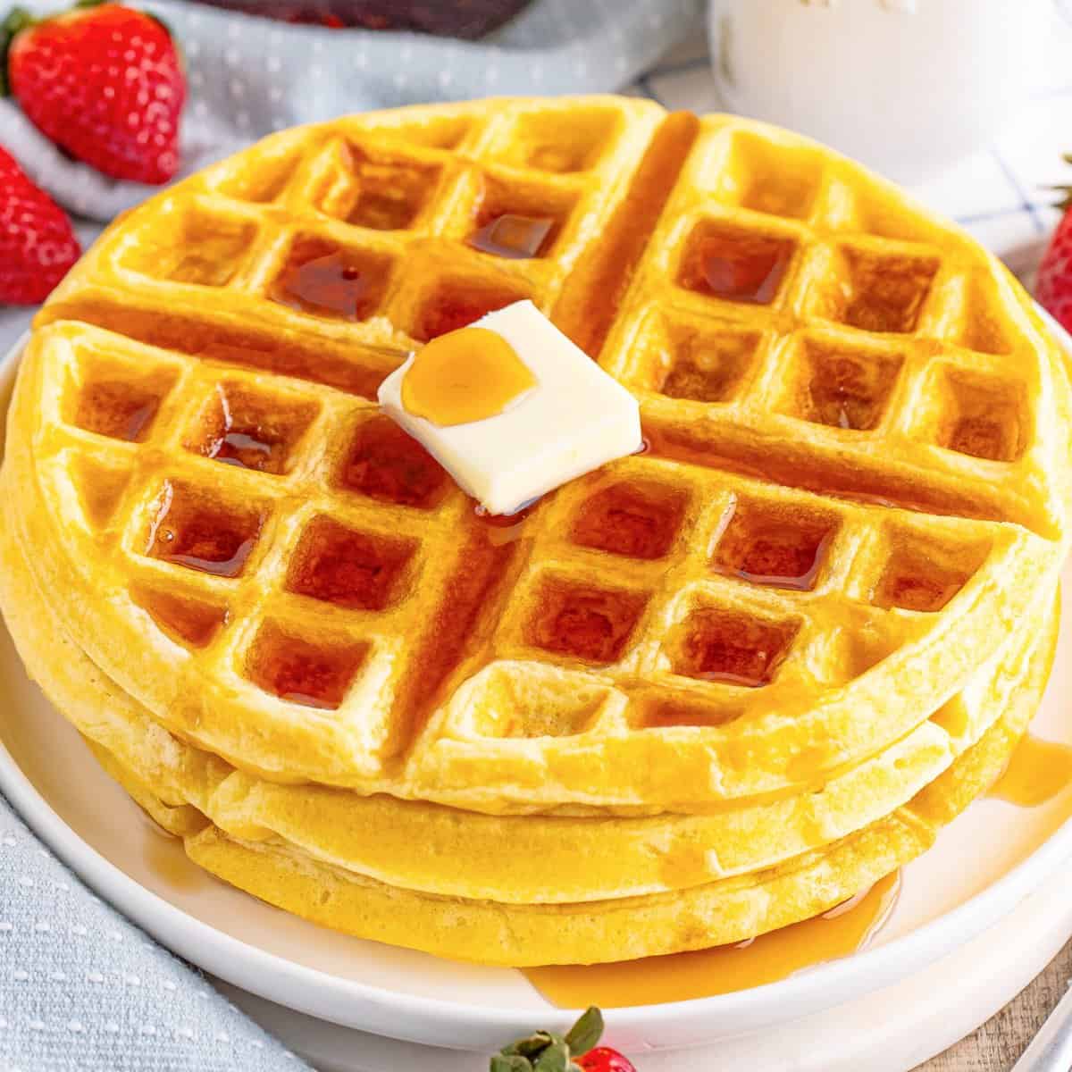 Looking down on a small stack of Buttermilk Waffles with a pad of butter on top and some syrup drizzled.