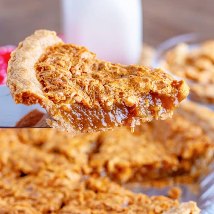 A slice of Peanut Pie being held over the rest of the pie.