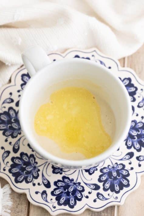 Butter being added to pancake mix in a mug.