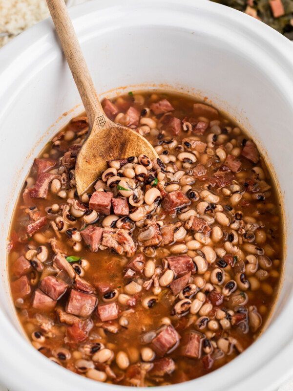 Black eyed peas in a white slow cooker with a wooden spoon in it.