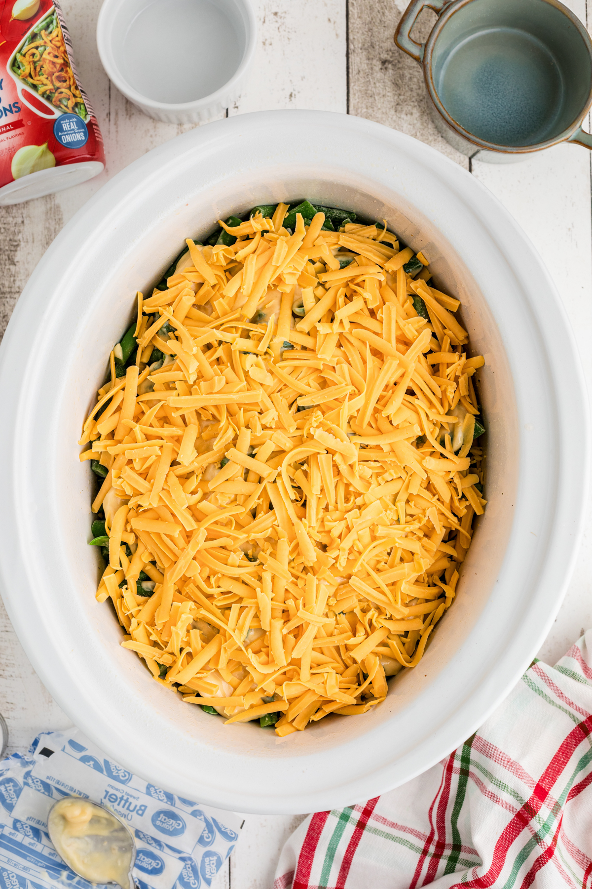 Shredded cheddar cheese sprinkled on top of ingredients in a crockpot.