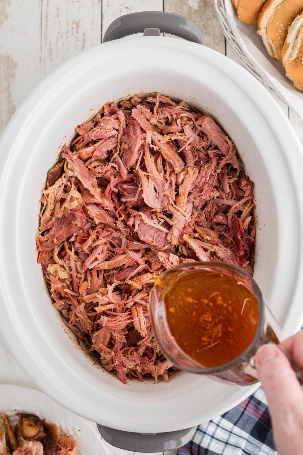 adding reserved cooking liquid to shredded ham in a crockpot.