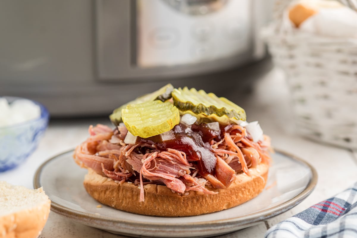 slow cooker pulled ham on the bottom of a hamburger bun with toppings.