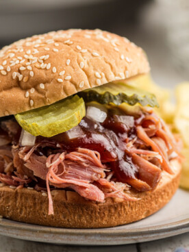 close-up of a slow cooker pulled ham sandwich with toppings on a plate.