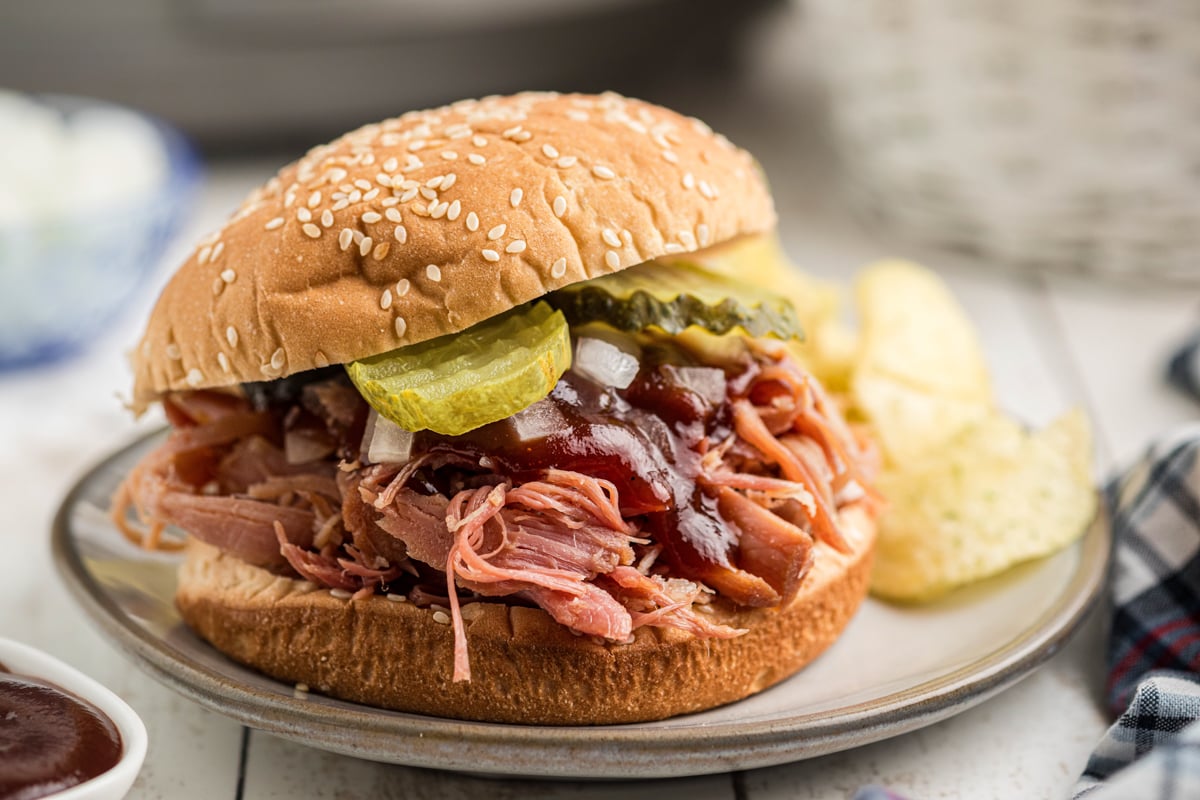 close-up of a slow cooker pulled ham sandwich with toppings on a plate.