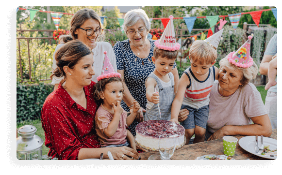 A photo of a family gathered around a table at a child's birthday party. The child is cutting the cake while everyone waits in polite anticipation.